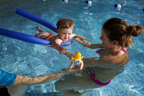 Mum with child in a swimming pool, child is reaching for a toy duck